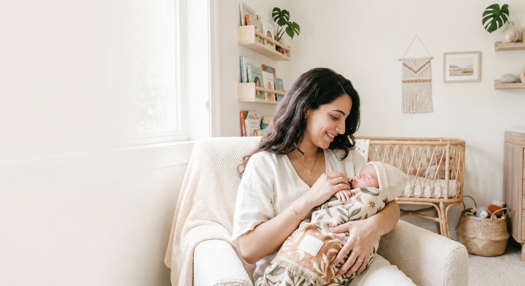 A smiling mother holding her newborn baby in a calm, sunlit nursery
